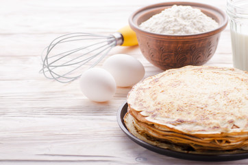 Stack of French crepes in frying pan on wooden kitchen table with milk eggs and flour aside