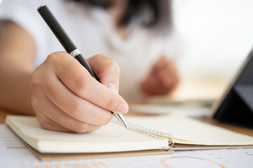 Close shot of businesswoman hands holding a pen writing something on the paper on the...