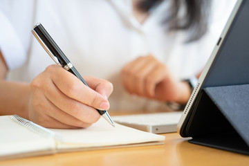 Close shot of businesswoman hands holding a pen writing something on the paper on the...