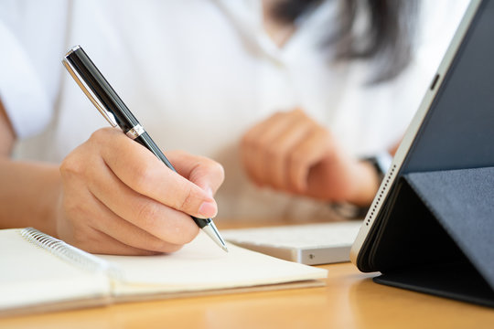 Close shot of businesswoman hands holding a pen writing something on the paper on the foreground in office. Recording concept. - Powered by Adobe