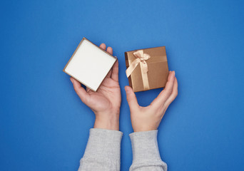female hand in a gray sweater holds open square cardboard gift box