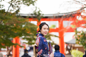 Fototapeta premium Geishas girl wearing Japanese kimono among red wooden Tori Gate at Fushimi Inari Shrine in Kyoto, Kimono is a Japanese traditional garment. The word 