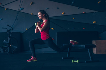 Slim fit muscular brunette woman exercise in gym, lifting weights and doing pilates. Picture with dark evening mood and film color grading.