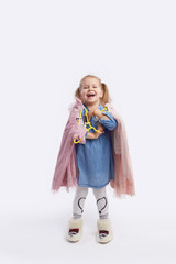 Little child girl chooses outfits for the holiday. Holds hangers with dresses in his hands. White studio background