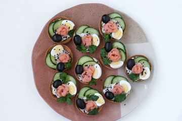Holiday tartlets with cheese, salmon, black olives, quail eggs and cucumbers on a plate on white background, Top view