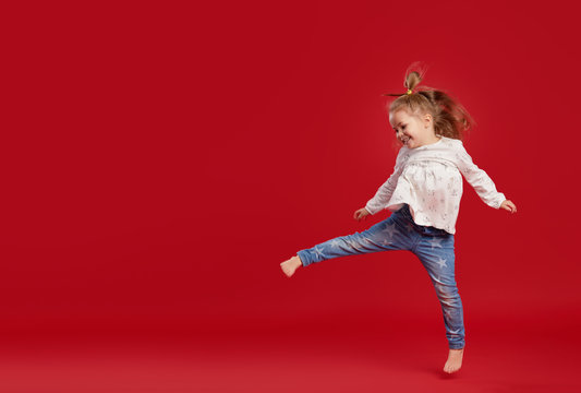 Happy childhood. Funny child girl jumping and having fun isolated on red background. Celebrating a vibrant carnival for kids, birthday party. True emotions. Space for text
