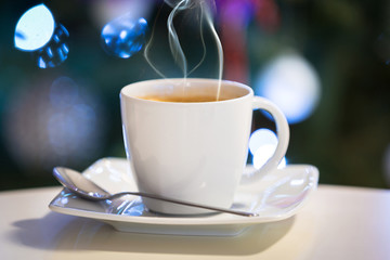 Cup of hot coffee on the table with christmas tree lights in background