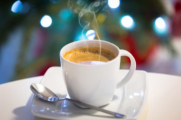 Cup of hot coffee on the table with christmas tree lights in background