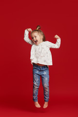 Happy childhood. Funny child girl jumping and having fun isolated on red background. Celebrating a vibrant carnival for kids, birthday party. True emotions. Space for text