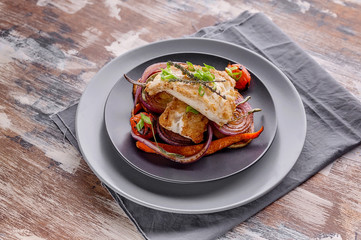 Appetizing cod filet with red onion and herbs: sage, rosemary and thyme, baked potatoes and carrots on a side dish in a gray plate on a gray napkin. Tasty and healthy sea fish