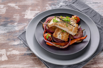 Closeup appetizing cod filet with red onion and herbs: sage, rosemary and thyme, baked potatoes and carrots on a side dish in a gray plate on a gray napkin. Tasty and healthy sea fish