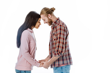 side view of happy young interracial couple holding hands with closed eyes isolated on white