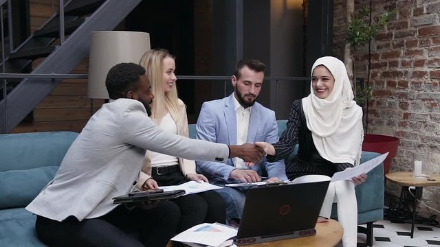 Friendly of four multiethnic colleagues team discuss important matter project using works papers and digital computer at workplace. Slow motion