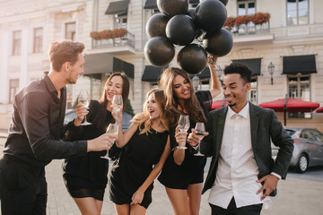 Handsome man in stylish suit telling joke while drinking champagne with friends. Outdoor portrait...