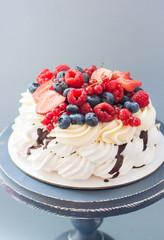 Meringue pavlova cake decorated with fresh berries, strawberries, raspberries, blueberries and red currant. 