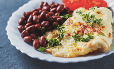 omelet with red beans and tomato in white plate on Dark grey black slate background