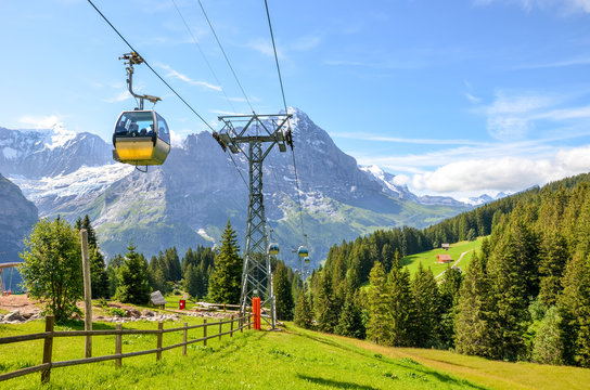 Yellow cable car in the Swiss Alps. Gondola going from Grindelwald to First in the Jungfrau area. Summer Alpine landscape with snowcapped mountains in the background. Transport tourists uphill