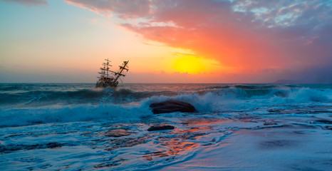 Fototapeta na wymiar Sailing old ship in stormy sea in the background dramatic sunset 