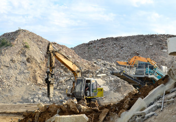 Obraz premium Salvaging and recycling building and construction materials. Excavator with hydraulic hammer work at landfill with concrete demolition waste. Reinforced concrete mobile shredder. Reuse concrete