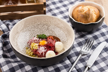 Appetizer Steak Tartare with bread bun and yolk on fabric napkin on wooden table
