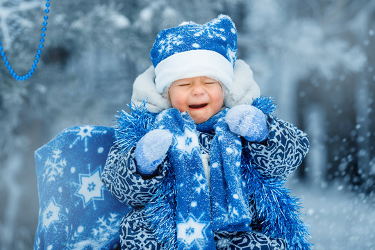 A child in a blue santa claus costume cries because snow flies into him. Christmas card, new year.  Autdoor games.