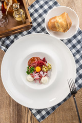 Appetizer Steak Tartare with bread bun and yolk on fabric napkin on wooden table