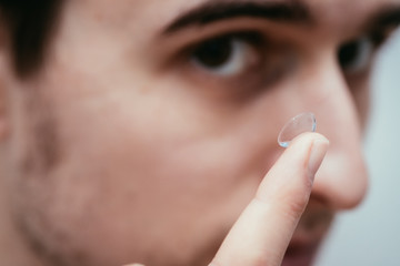 Contact lens lying on a male finger, macro close up. Customer, patient or eye in the blurry background.