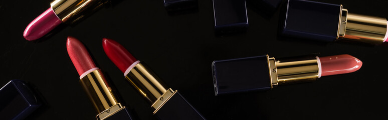 top view of assorted lipsticks in luxury tubes scattered isolated on black, panoramic shot