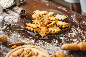 Cooking Christmas cookies at home on the brown table. Plate with freshly baked cookies in the shape of Christmas trees