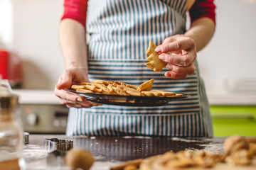 Cook housewife making cookies at home on a kitchen. Woman holding freshly baked cookies in the shape of Christmas trees