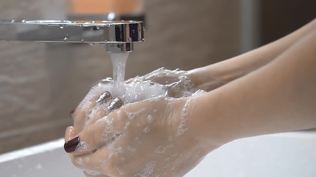 Woman washing her hands with soap in the bathroom. Wash off the soap from the hands under the water stream from tap. Slow motion.