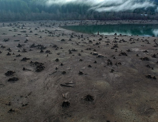 Dramatic aerial Photography of Rattlesnake lake surrounded by tree trumps and clouds reflecting off the shallow lake in the fall with the fog covered mountains in near distance in Washington State