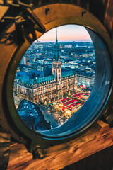 Top view of illuminated Christmas market on townhall square in advent time, Hamburg, Germany. Porthole window framed view