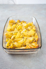 Oven-baked potatoes with olive oil, garlic and thyme in a glass form on a light textured background.