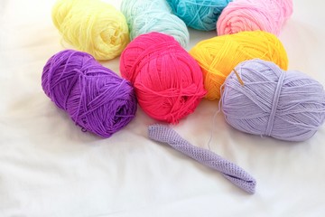 Colorful yarn material with golden crochet hook in progress of creating yarn thread textile knitting. On white fabric background with copy space for text. Hobby, lifestyle concept.