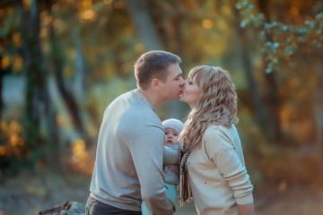 Fototapeta premium Family outdoors feel the love of their child hugging and kissing him in the autumn forest on a walk.