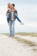 Happy young man giving piggyback ride to woman on trail at field