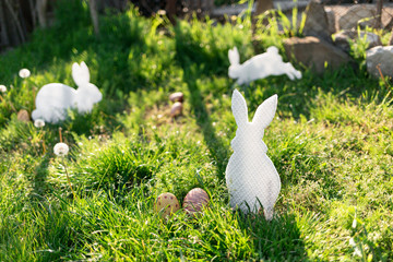The concept of Easter holidays. Decorative Handicrafts handmade in the form of different white rabbits, located next to the painted eggs. Green grass in the background. Copy space