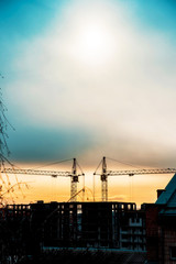 Abstract image of a pair of construction cranes on a sunrise background (progress, lower mortgage rates, falling house prices - concept)