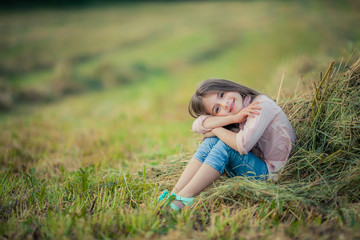 Fototapeta premium A girl sits in a field near a pile of freshly mown green hay.