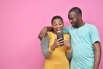 Obraz premium two young african friends, boy and girl, looking excited while viewing something on their smartphone together