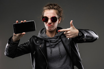 cheeky girl in glasses with a phone with a mockup on a black wall