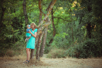Photo of a woman with a child in her arms in full growth in the summer forest outdoor.