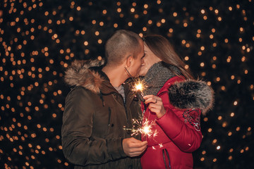 Young happy couple having fun outdoors in winter before Christmas with sparklers in hands