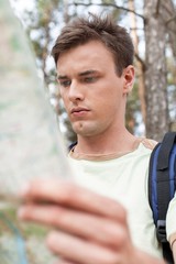 Handsome young man with backpack reading map in forest