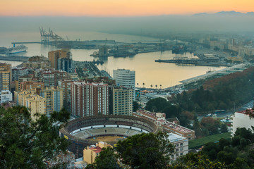 Sunset on the Spanish Mediterranean coast. View of the center of the city of Malaga on the Costa del Sol with illuminated buildings, trees, street lamps, port, ships