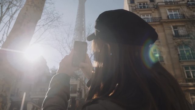 Rear view happy beautiful tourist woman taking smartphone video of Eiffel Tower in Paris to share online slow motion.