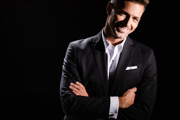 Smiling businessman with crossed arms looking at camera isolated on black