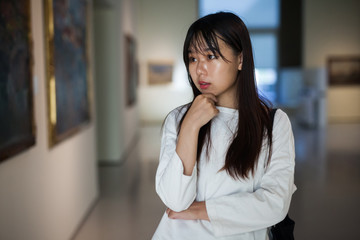 Chinese female visitor looking at artwork painting in the museum