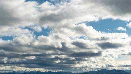 Fototapeta premium Colorful evening clouds on a bright blue sky above the peaks of the mountains in the distance. Beautiful landscape background